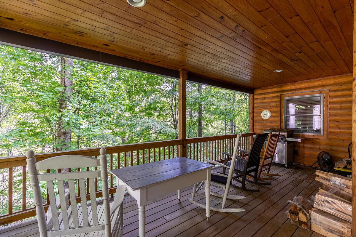 This exterior image features a cozy porch with classic rocking chairs, a wooden table, a log stack, and lush greenery. The setting is ideal for gathering after a day outdoors—perfect for sharing stories, warming up, or enjoying a hot drink surrounded by nature.