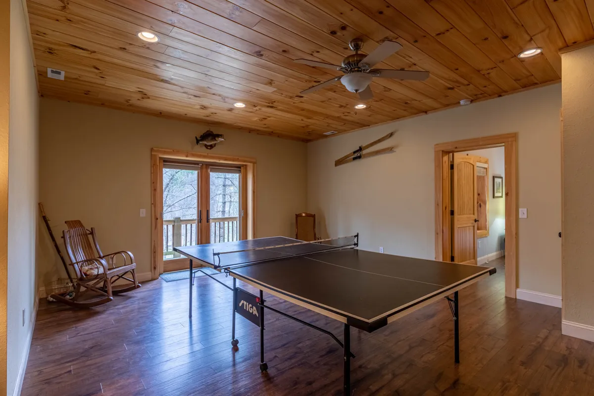 This interior game room features a ping pong table, a comfortable rocking chair, and double doors that lead outside. The space is clearly designed for playful gatherings, friendly competition, and easy access between indoor and outdoor activities.