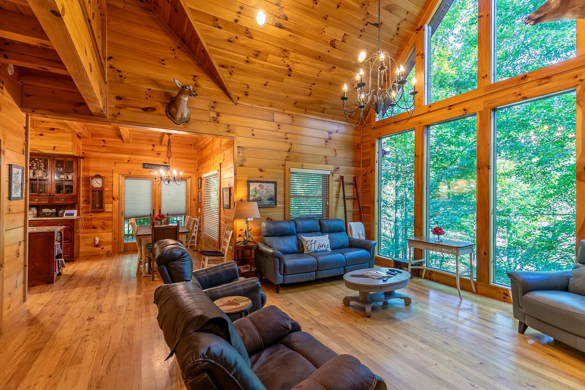 This image features a comfortable seating area with large windows that open up to serene views of nature. The rustic wooden ceiling and walls, paired with a chandelier, create a welcoming, lodge-like atmosphere that subtly hints at the surrounding mountain landscape.