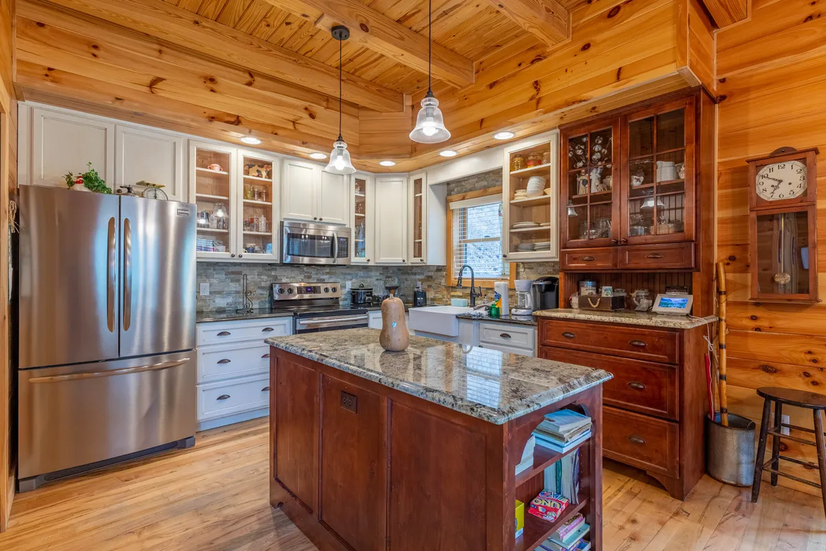 A cozy kitchen scene featuring a granite-topped island, wooden cabinetry, multiple appliances, and glass-front cabinets. The space is arranged for both serious cooking and casual gatherings, with room for helpers to participate.