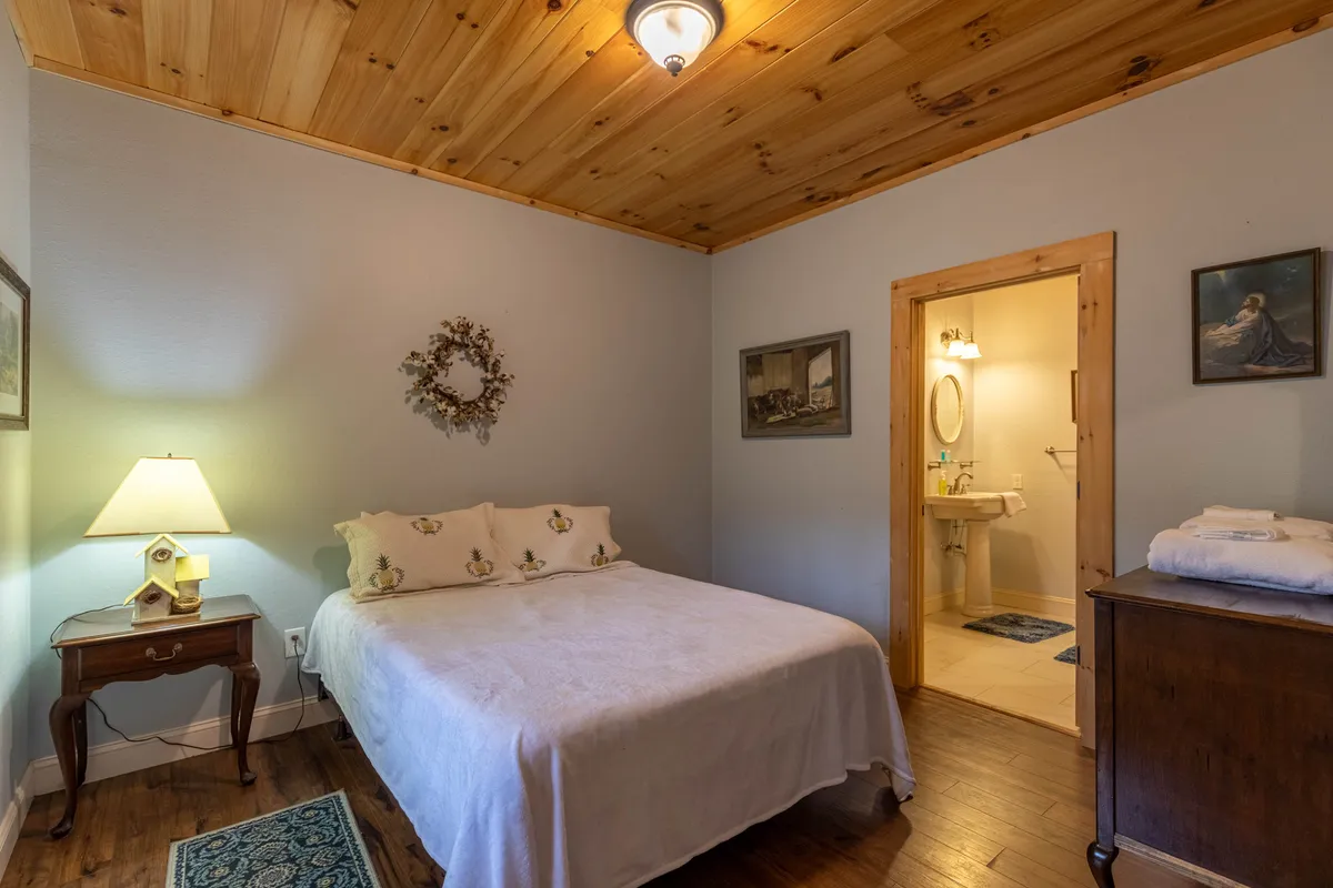 A serene bedroom with white linens, a nightstand with a softly glowing lamp, and gentle, decorative touches like a wreath and paintings. The space feels calming and restorative.