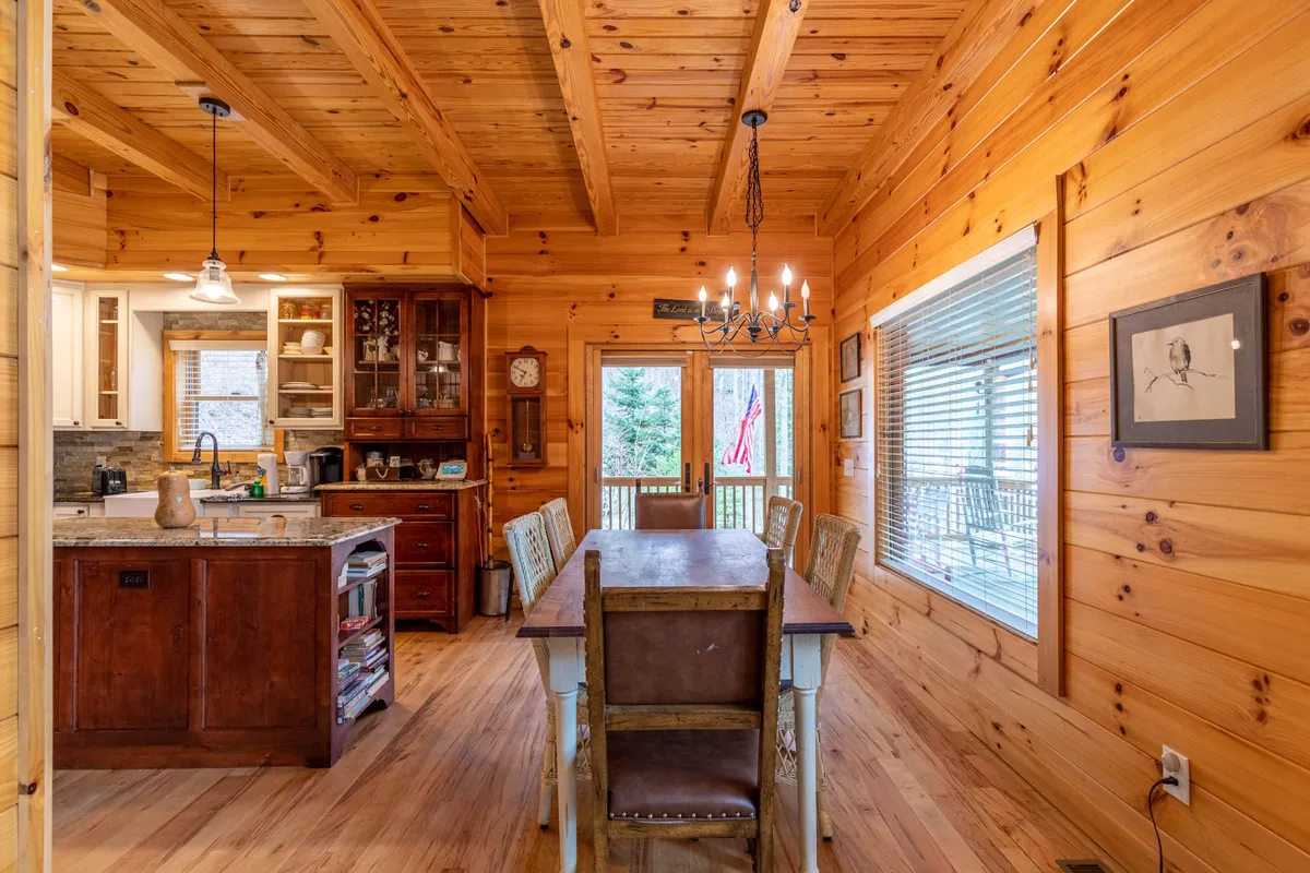 A bright and welcoming dining area, featuring a large wooden table, kitchen island, and expansive windows that let in natural light. The scene embodies the communal dining experience and offers a glimpse of the outdoors, enhancing the sense of connection.